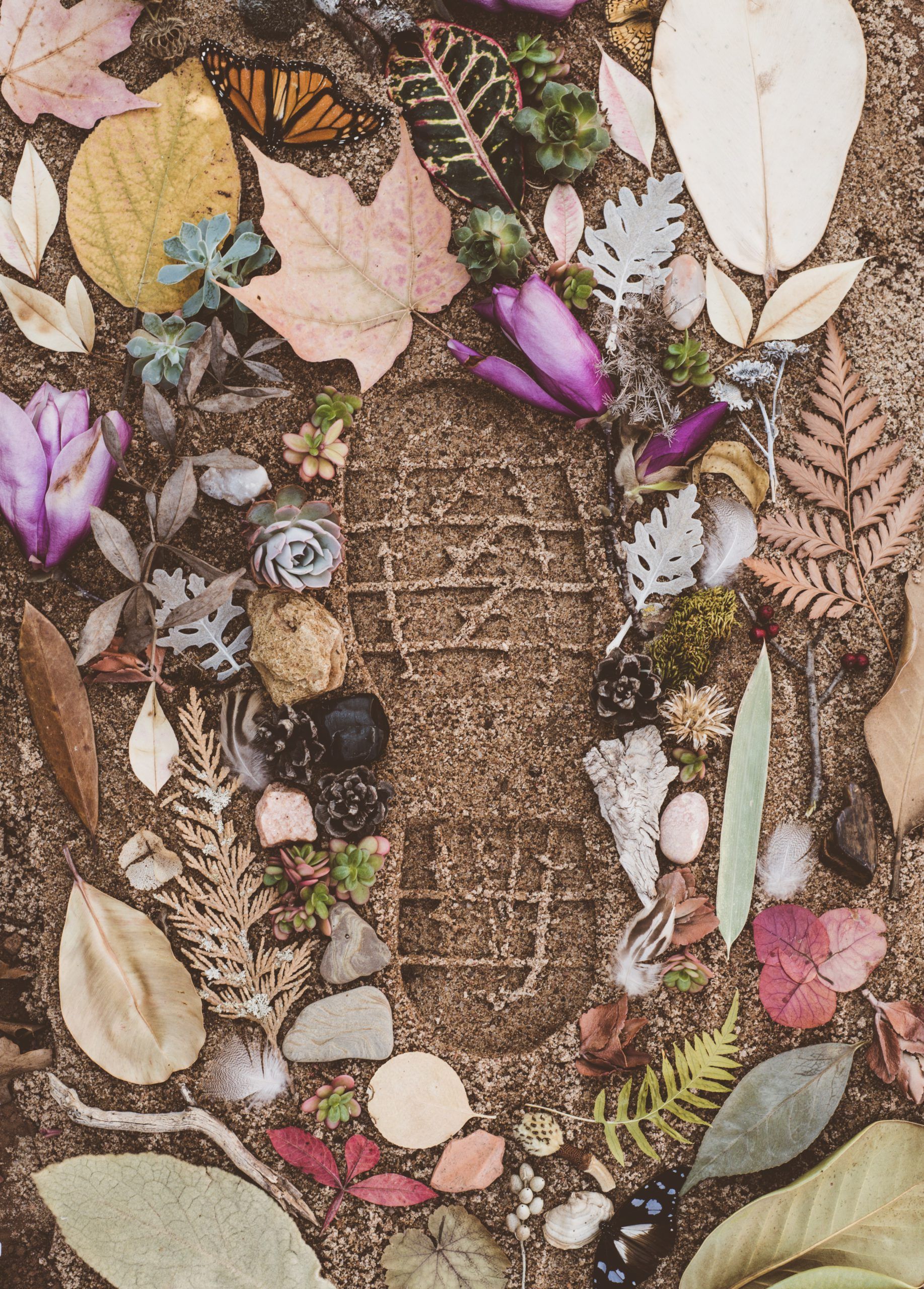 Empreinte de pied sur le sable entourée de fleurs et de feuilles colorées